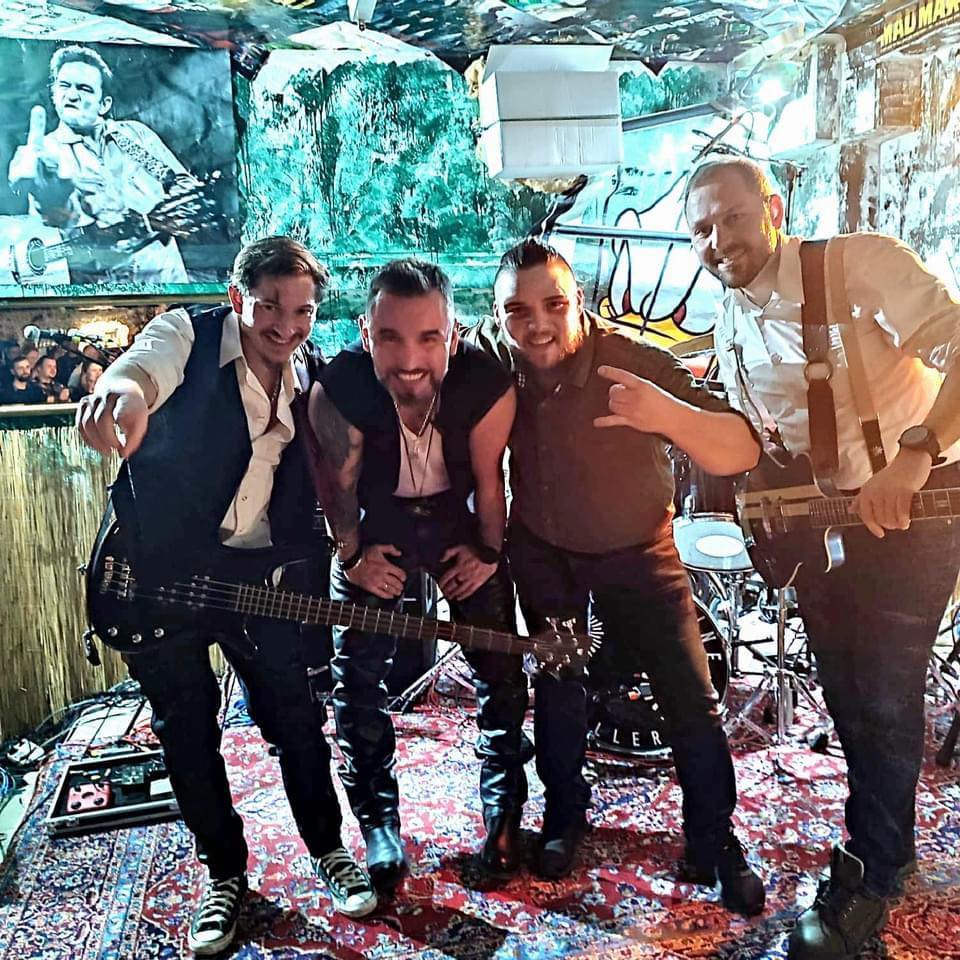 Four guys on the stage, two of them holding guitars, laughing and posing in front of the camera
